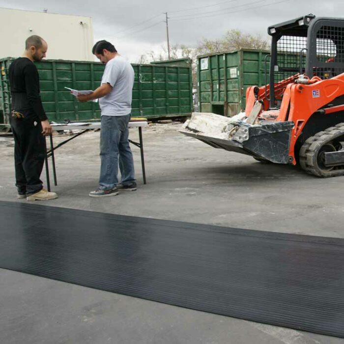 Black corrugated rib mat splayed out diagonally with people standing next to it outdoors