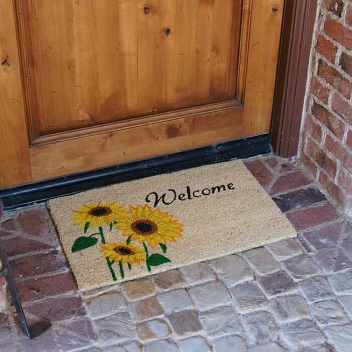 Welcome mat with sunflower design in front of brown door