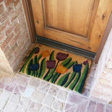 Handmade doormat with tulip garden design in front of light brown door