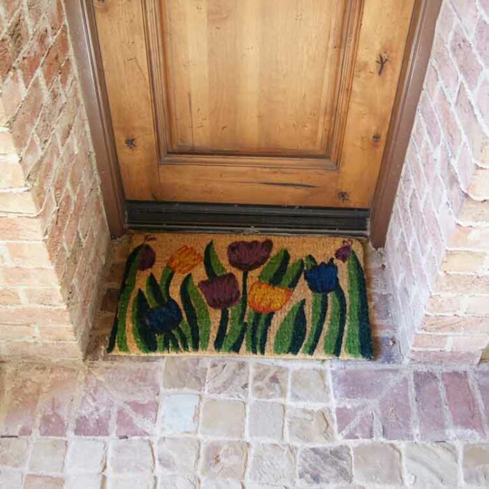 Handmade doormat with tulip garden design in front of light brown door
