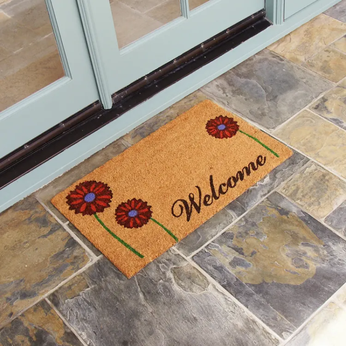 brown door mat with a red daisy design in front of white double doors