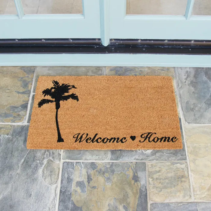 Beach themed welcome home mat with picture of tree in front of white double doors