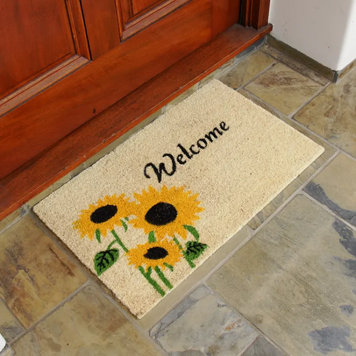 Welcome mat with sunflower design in front of red door