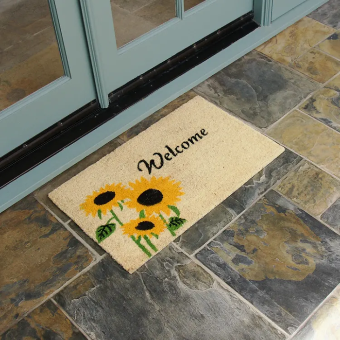 Welcome mat with sunflower design in front of white double door