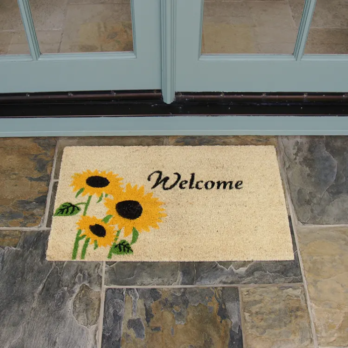 Welcome mat with sunflower design in front of white double door