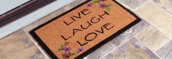 Brown live laugh love mat with black outline in front of white door tilted shot