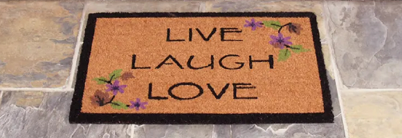 Brown live laugh love mat with black outline in front of white door
